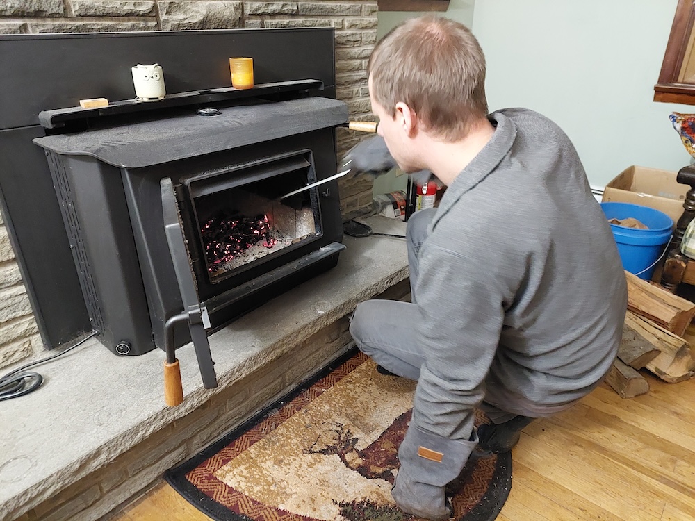 Kris moving hot coals to one side inside his wood stove.