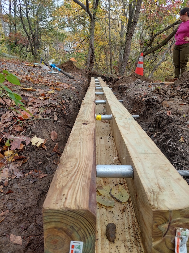 Open-top box culvert sits in a trench dug into the road.
