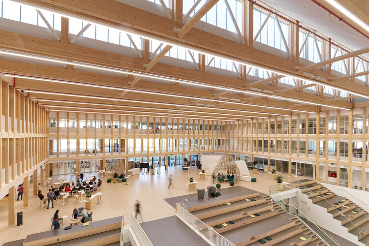 View of a large open area for people to congregate in made up of mass timber floor panels, trusses to support the roof, and posts to support three floors surrounding the open area.