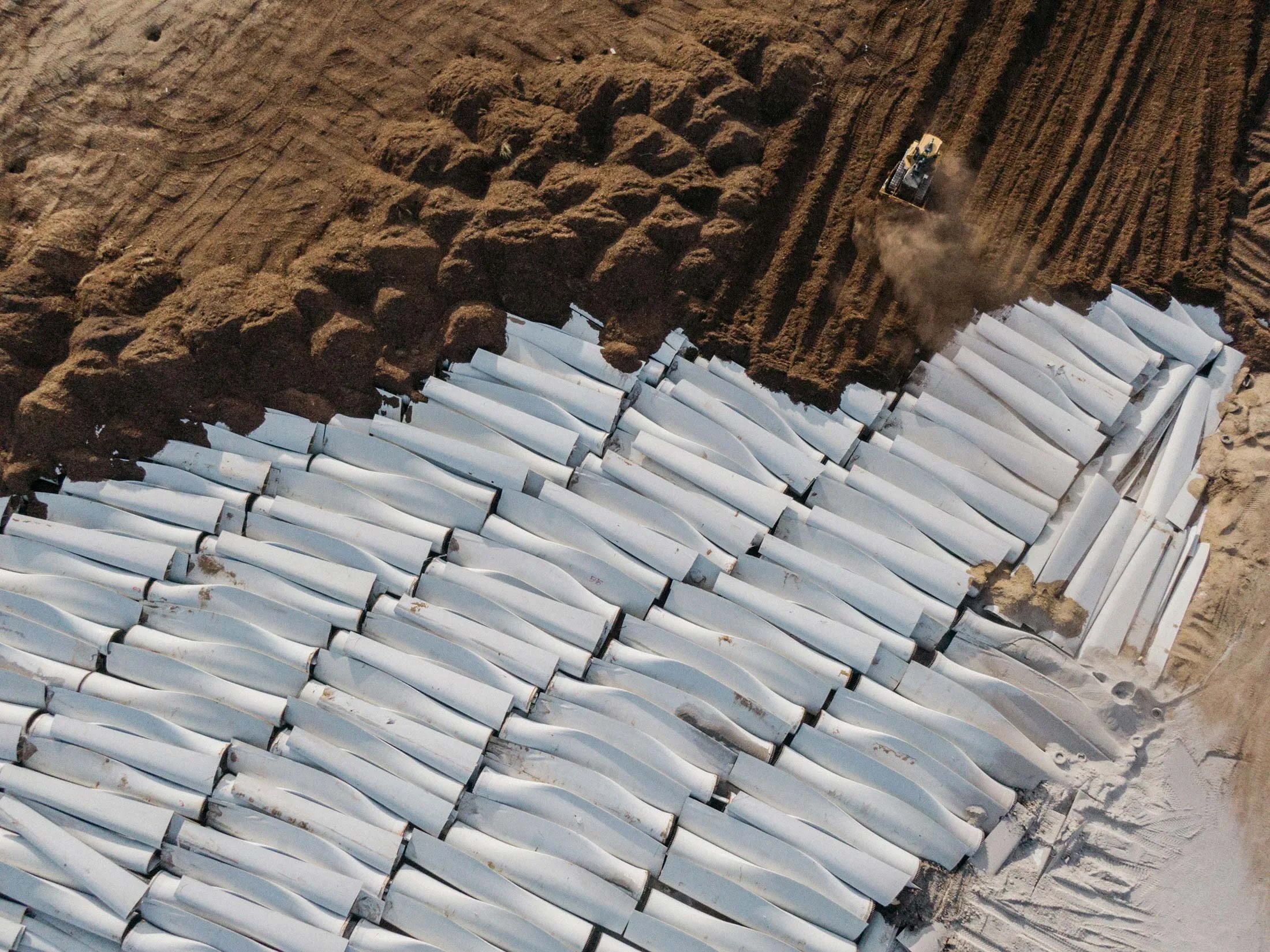 Picture of discarded wind turbine blades piled in rows at a site.